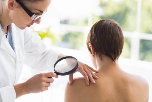 Doctor examining woman back with magnifying glass at clinic